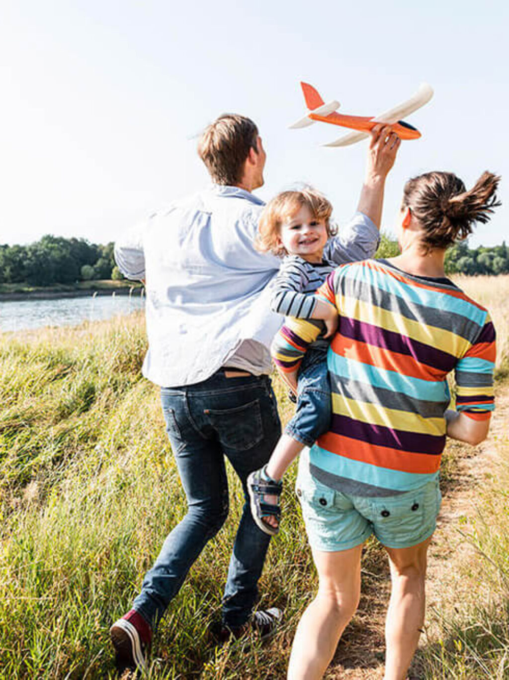 Famiglia corre nei campi. Padre tiene un aeroplano in mano e il bambino sorride felice in braccio alla mamma