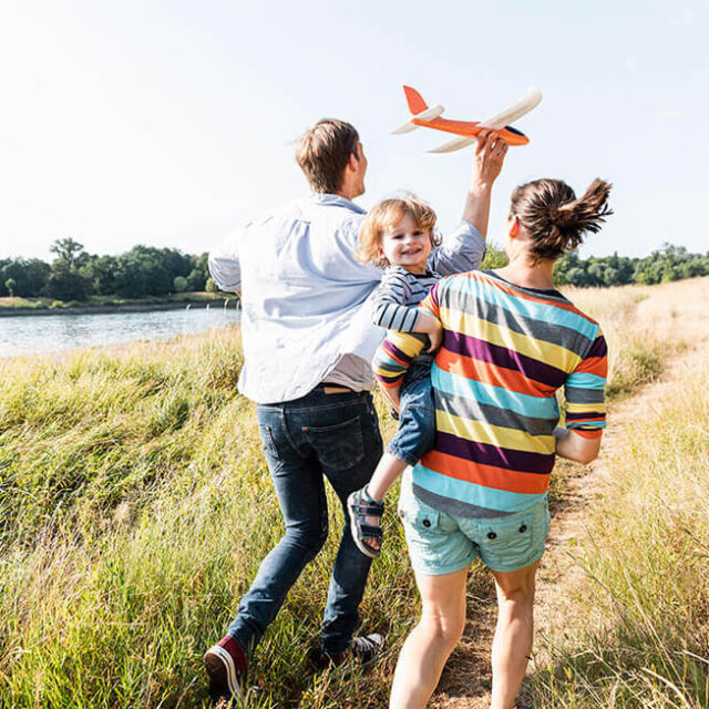 Famiglia corre nei campi. Padre tiene un aeroplano in mano e il bambino sorride felice in braccio alla mamma