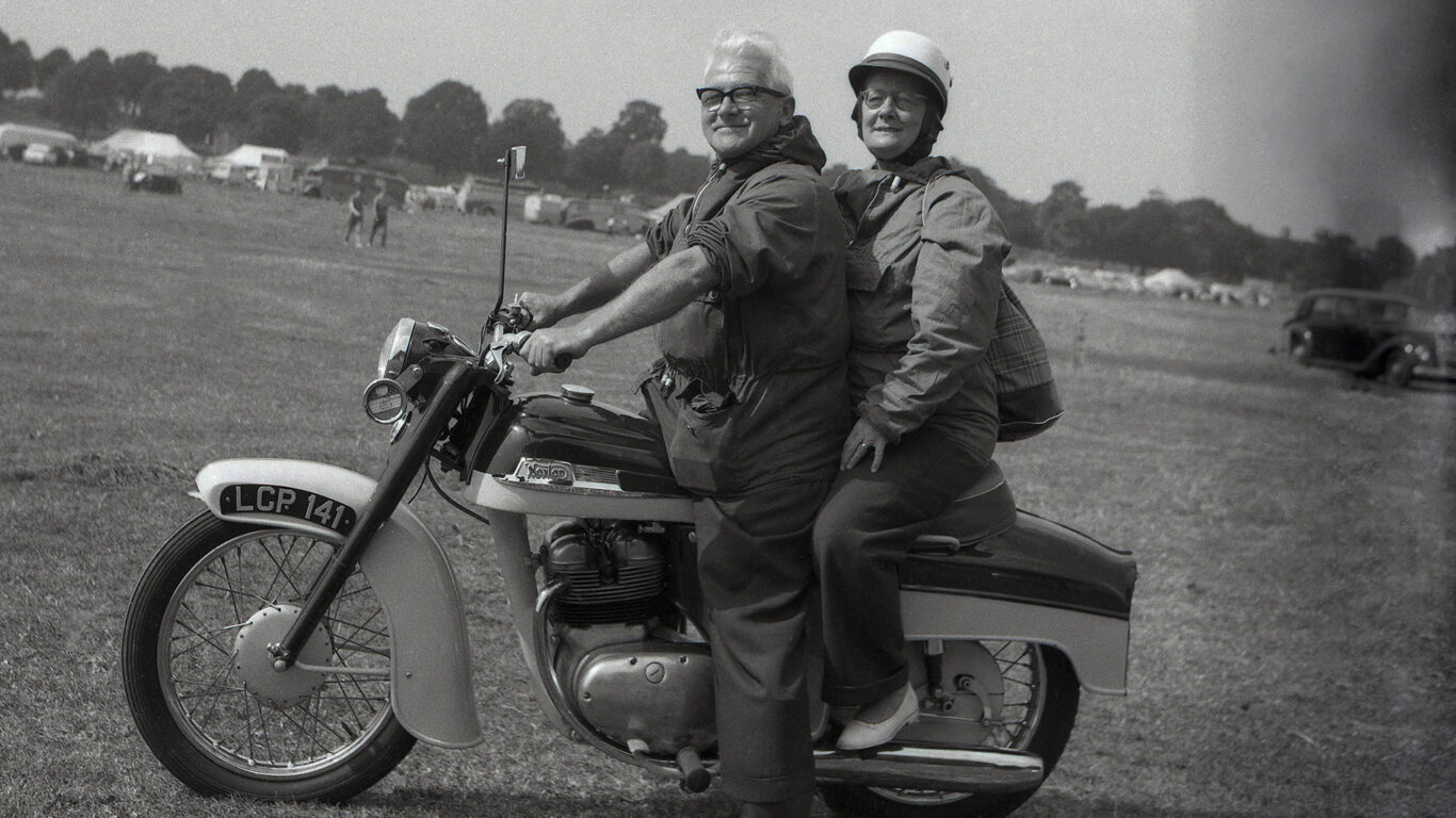 Coppia pensionati su motocicletta in un campo erboso.