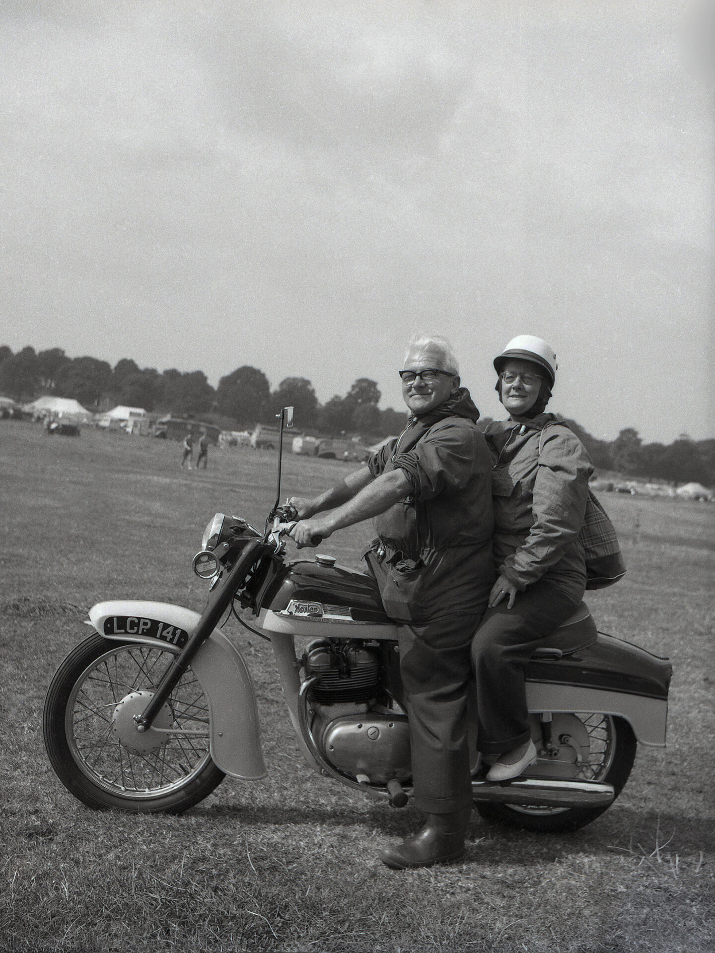 Coppia pensionati su motocicletta in un campo erboso.