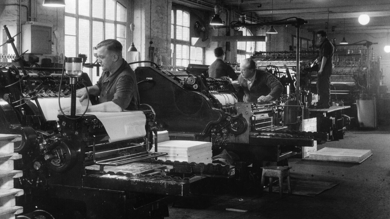 Interno copisteria anni 50. Tre operai lavorano sulle macchine.