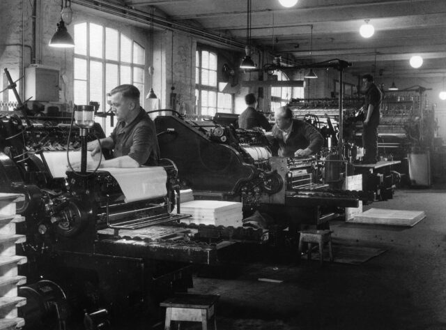 Interno copisteria anni 50. Tre operai lavorano sulle macchine.